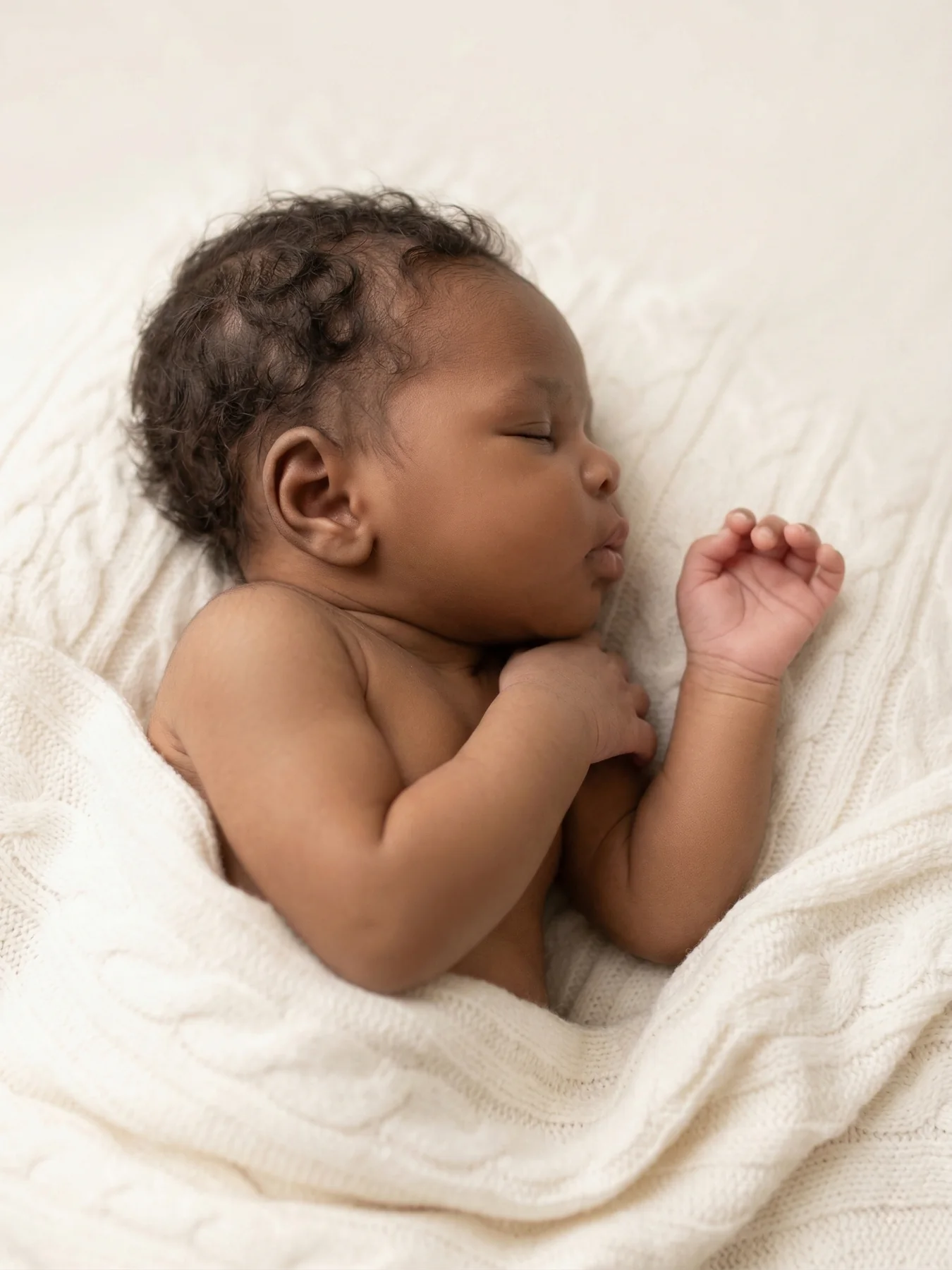 A sleeping newborn resting on a soft cream blanket
