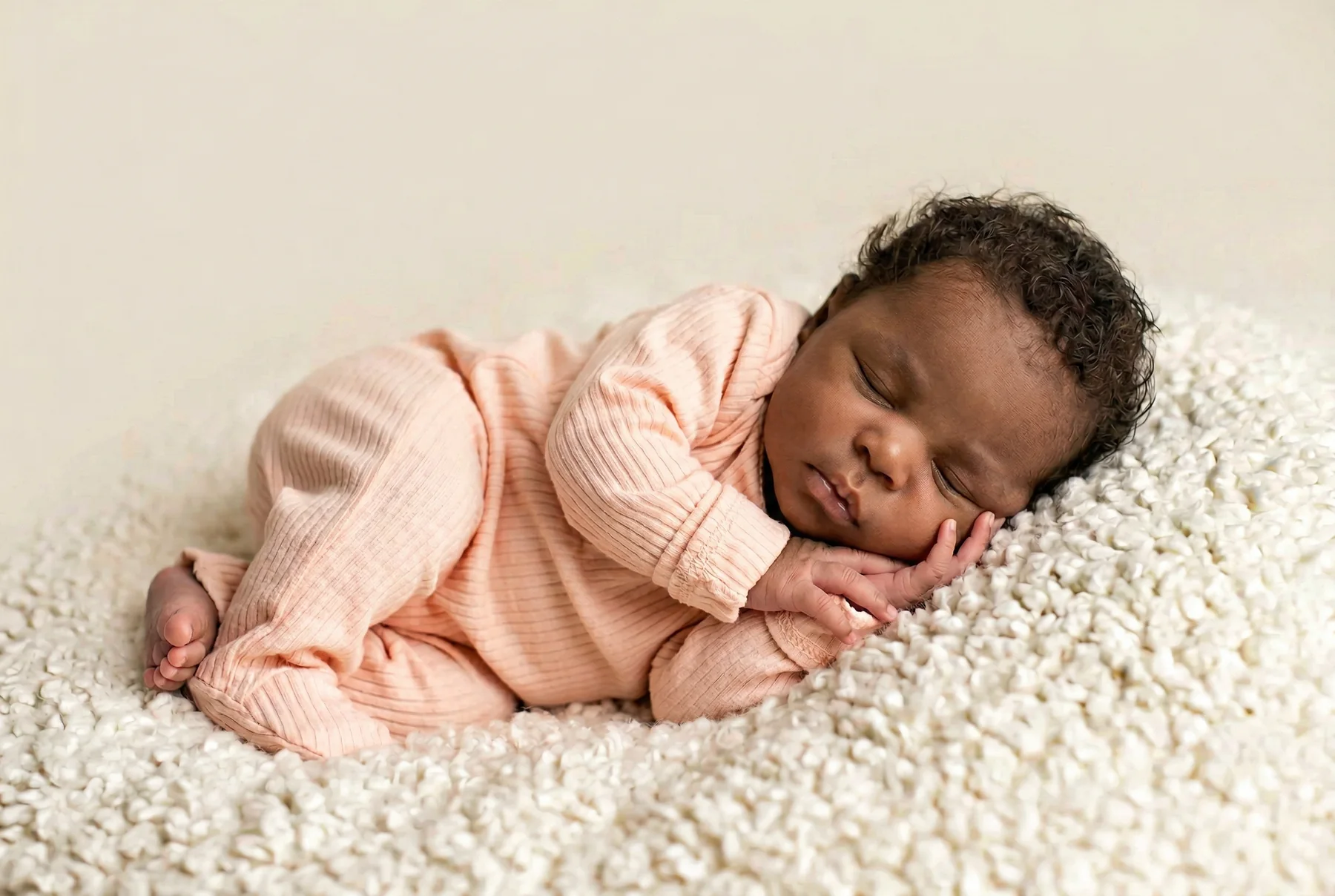 A newborn wearing a blush-pink knit outfit on a textured blanket