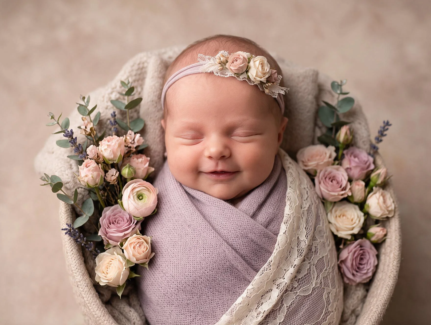 A smiling newborn wrapped in lavender and framed by flowers