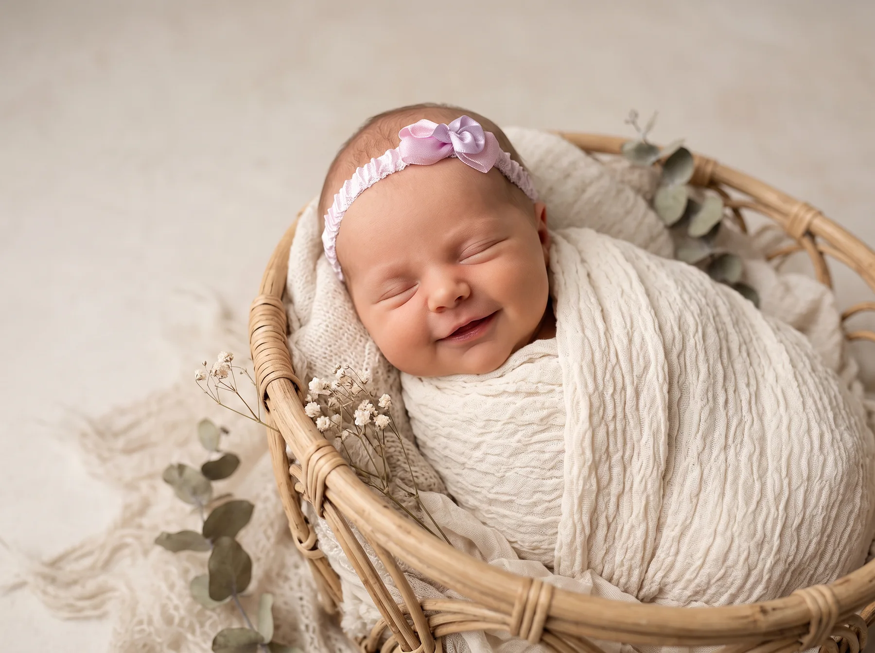 A smiling newborn wrapped in cream inside a woven basket