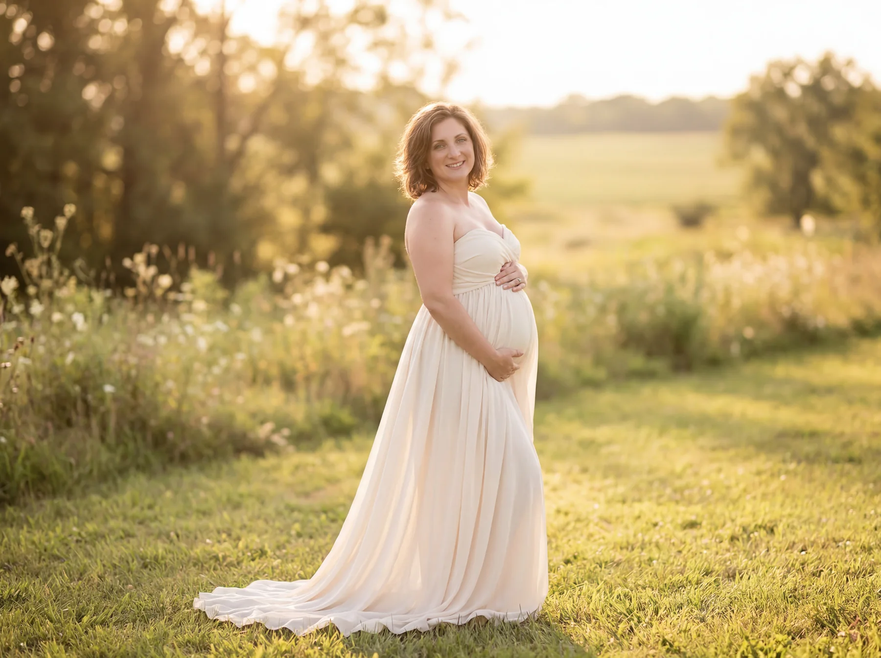 An expectant mother in a flowing cream dress in a sunlit meadow