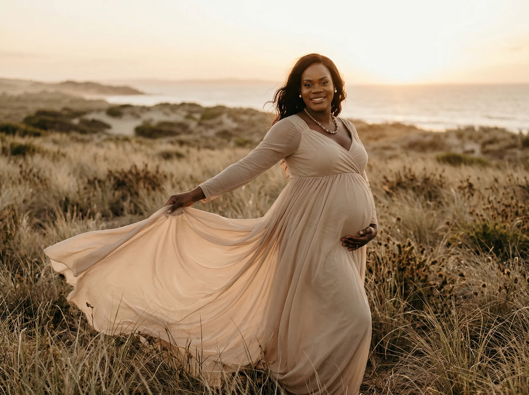 An expectant mother in a flowing cream dress among seaside dunes