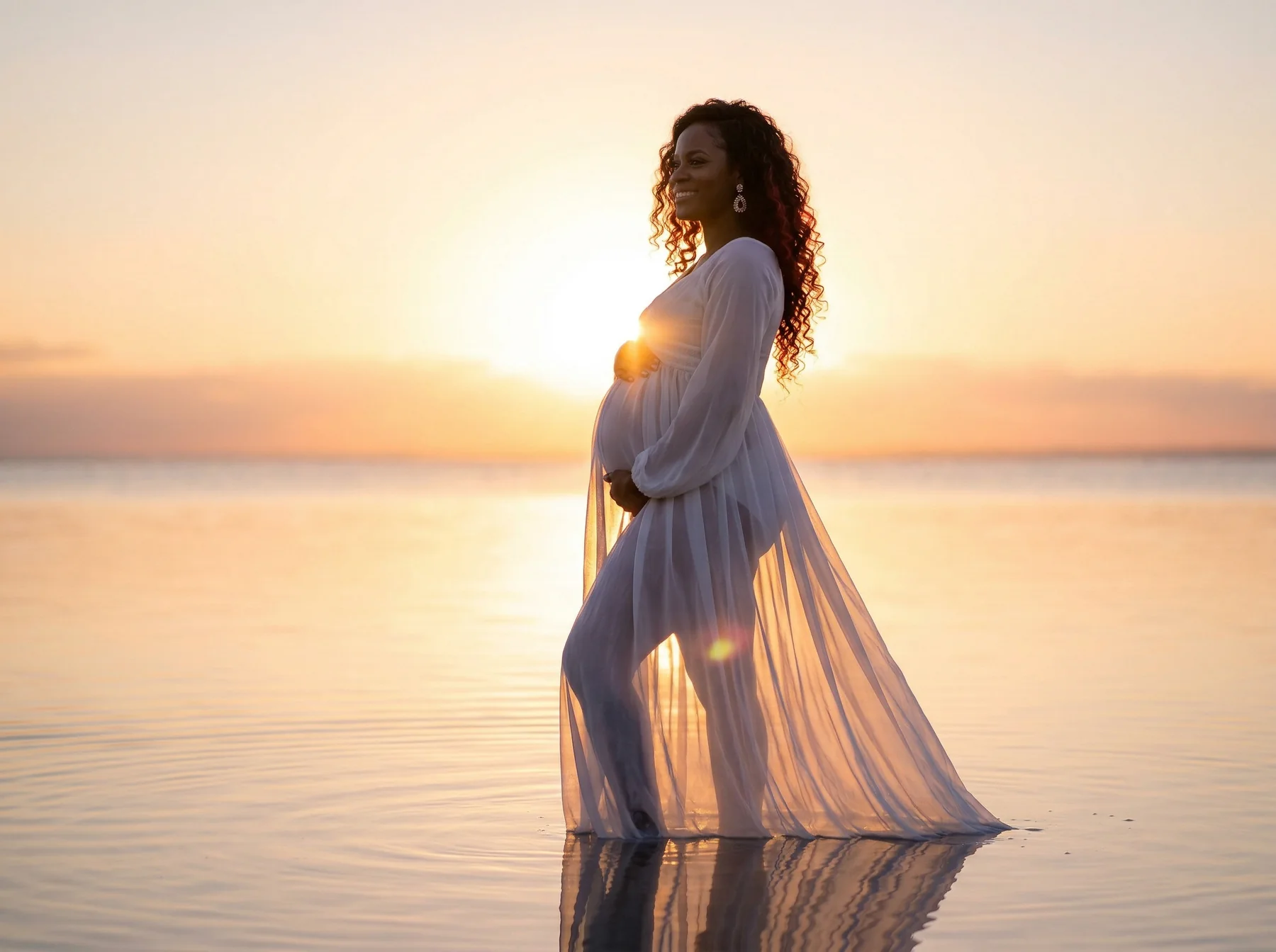 An expectant mother silhouetted against a sunrise over calm water