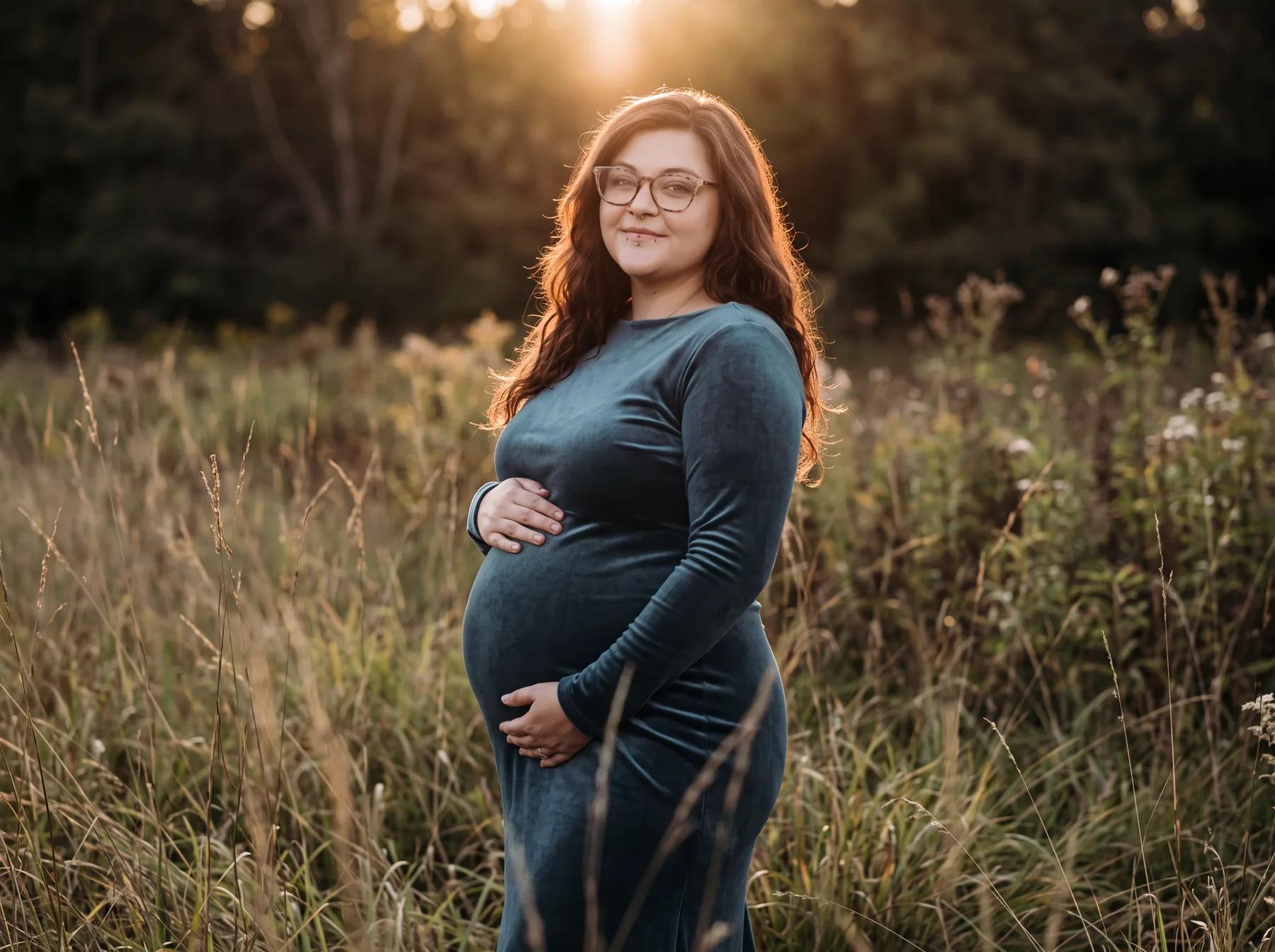 An expectant mother in a dark green dress standing in a warm meadow