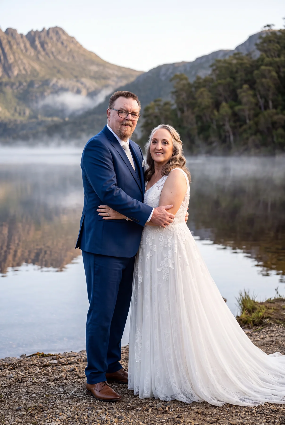 A bride and groom embracing beside a misty mountain lake